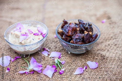 Close up shot of popular Indian & Asian Khajor dudh or dates milk in a transparent glass bowl along with raw dates and some cut in milk in a separate bowl on a brown colored surface or background. photo