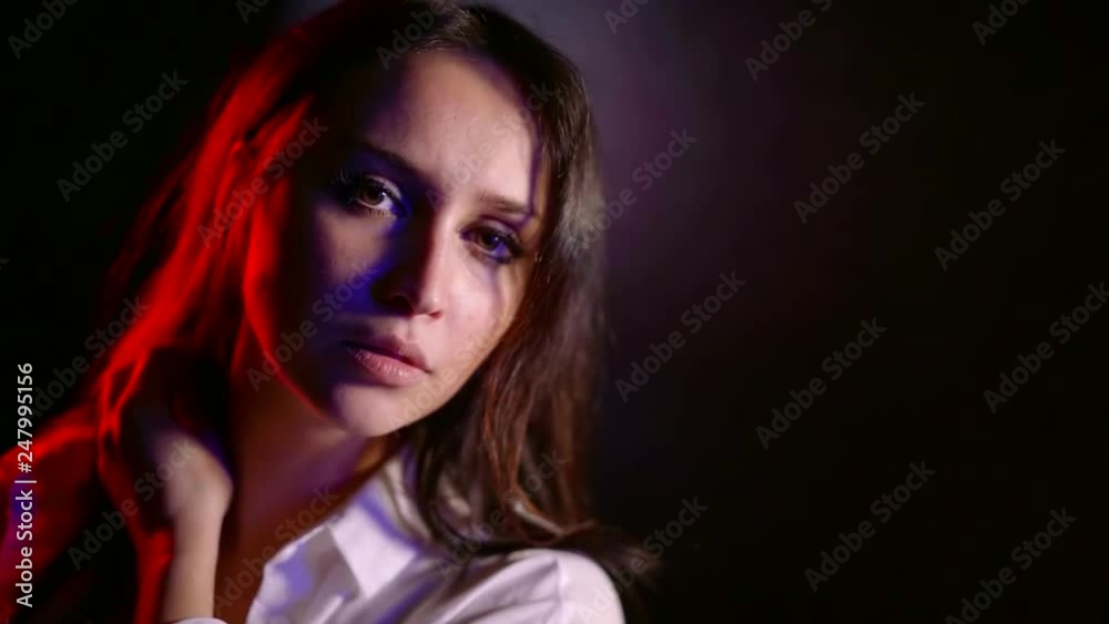 charming young woman with dark straight hair is looking at camera in dark studio with colored soffit charming young woman with dark straight hair is looking at camera in dark studio with colored soffit