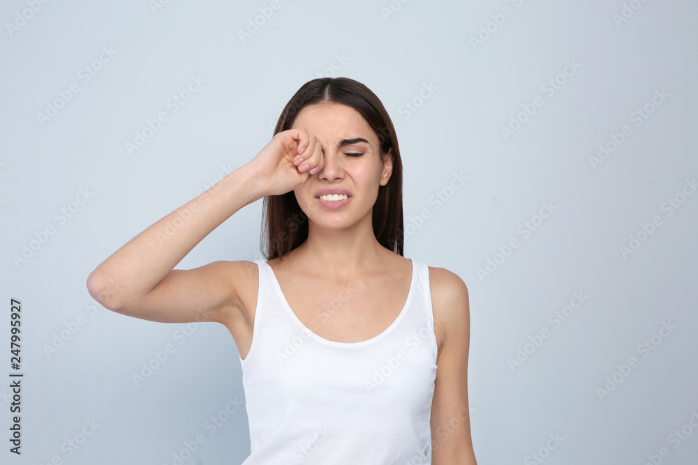 Young woman rubbing eye on light background. Annoying itch Young woman rubbing eye on light background. Annoying itch