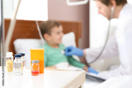 Table with medicaments and doctor examining little child in hospital
