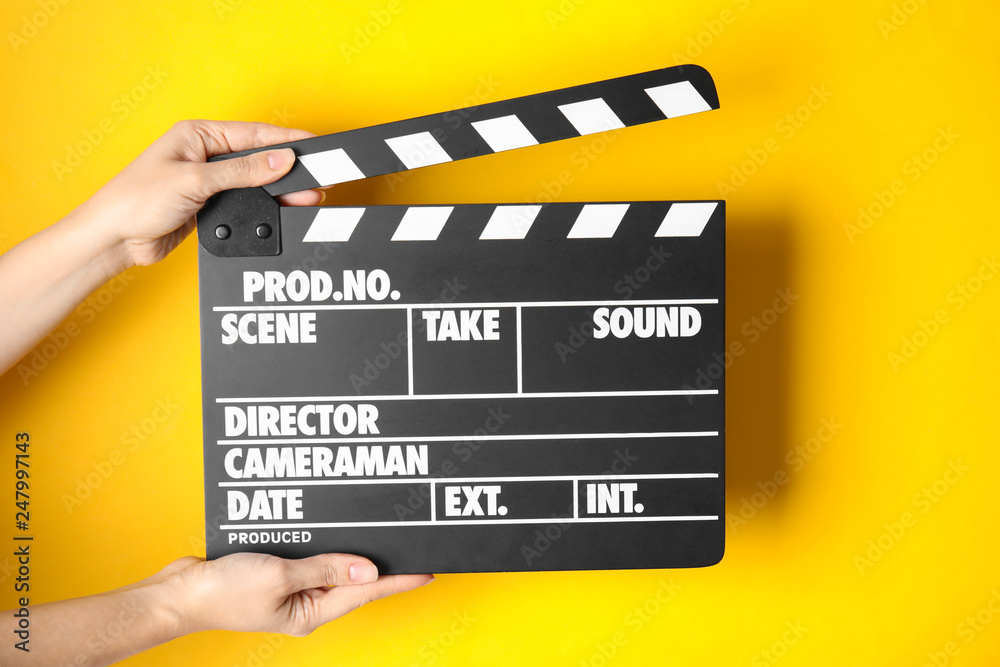 Woman holding clapperboard on color background, closeup. Cinema production