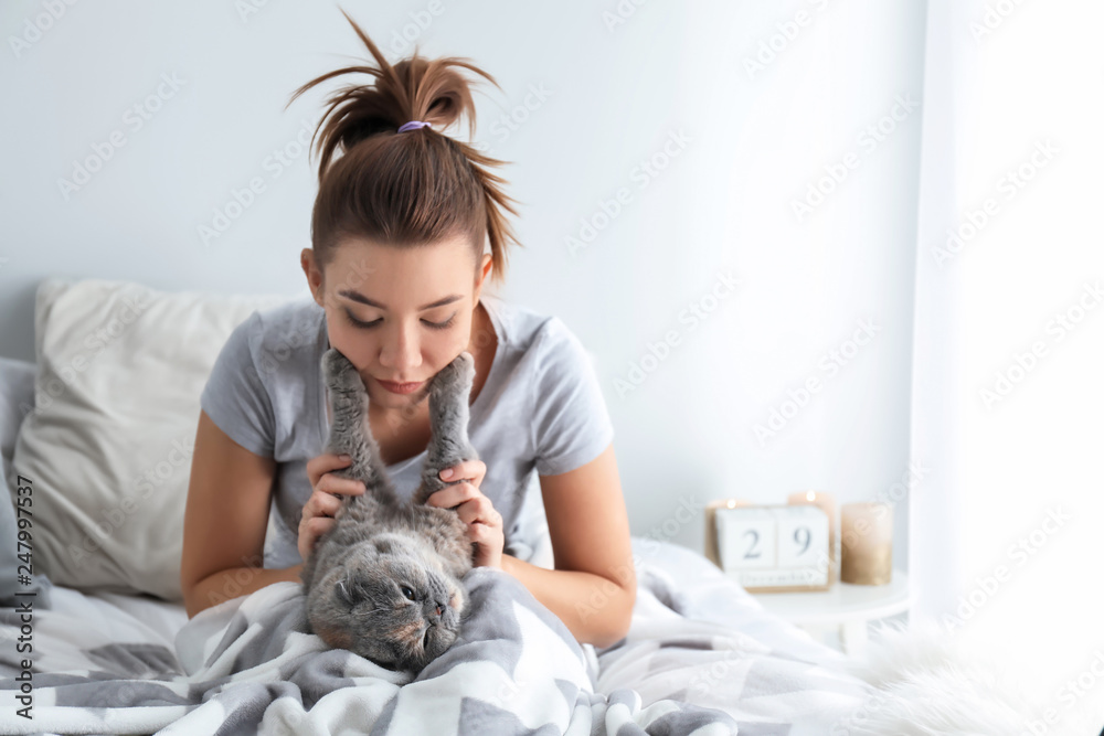 Young woman with cute cat resting on bed at home Young woman with cute cat resting on bed at home