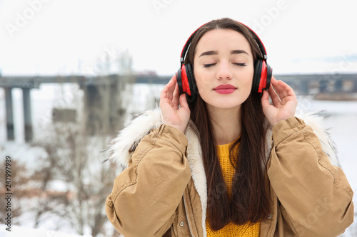 Beautiful young woman listening to music with headphones outdoors. Space for text