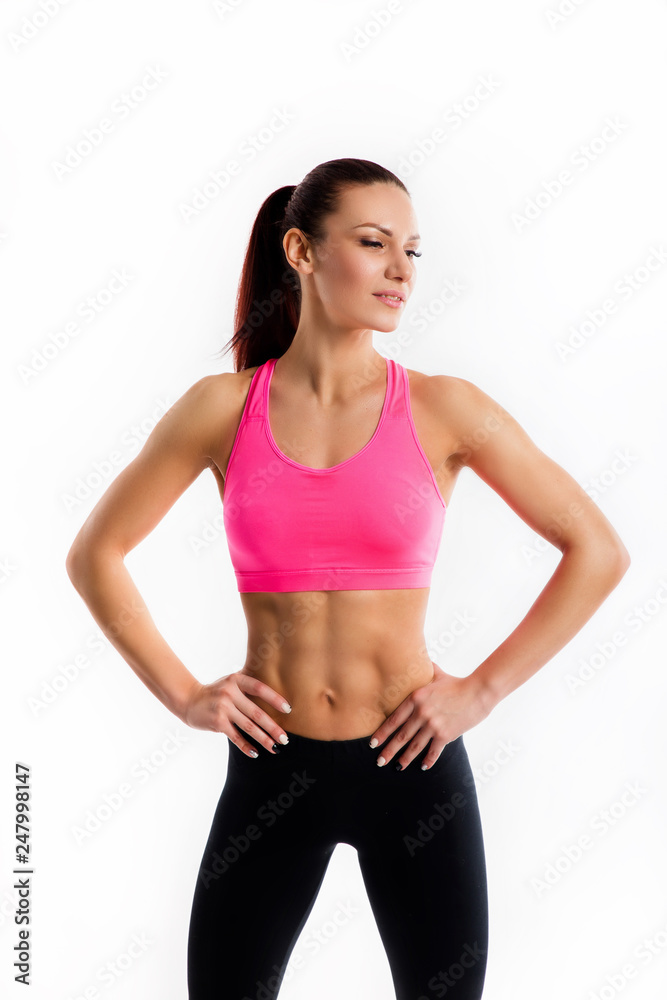 Attractive young woman in sportswear posing on white background. Healthy female model with muscular body in studio.
