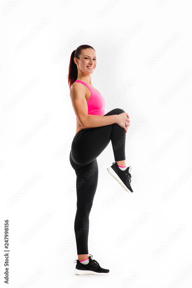 Young fitness woman doing stretching her legs. Photo of muscular woman in fashionable sportswear on white background. Strength and motivation. Young fitness woman doing stretching her legs. Photo of muscular woman in fashionable sportswear on white background. Strength and motivation.