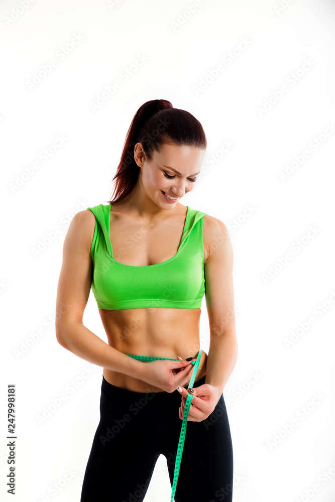 Attractive female bodybuilder measuring her waist with measurement tape. Photo of young woman in sportswear on white background. Attractive female bodybuilder measuring her waist with measurement tape. Photo of young woman in sportswear on white background.