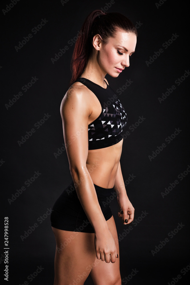 Strong woman bodybuilder with perfect abs, shoulders, biceps, triceps and chest. Photo of sporty young woman on black background.