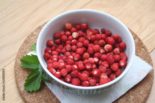 Fresh wild strawberries in a bowl on wooden table