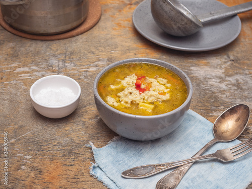 Soup with dumplings in a deep gray plate on a rustic table. In the background is a saucepan with soup, an old ladle on a plate. photo