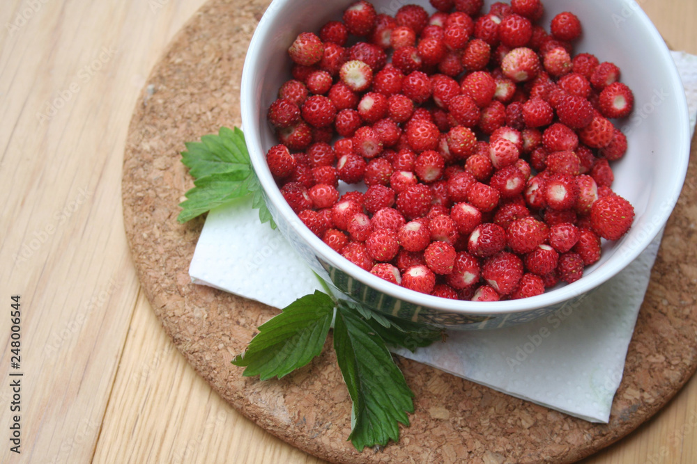 Fresh wild strawberries in a bowl on wooden table Fresh wild strawberries in a bowl on wooden table