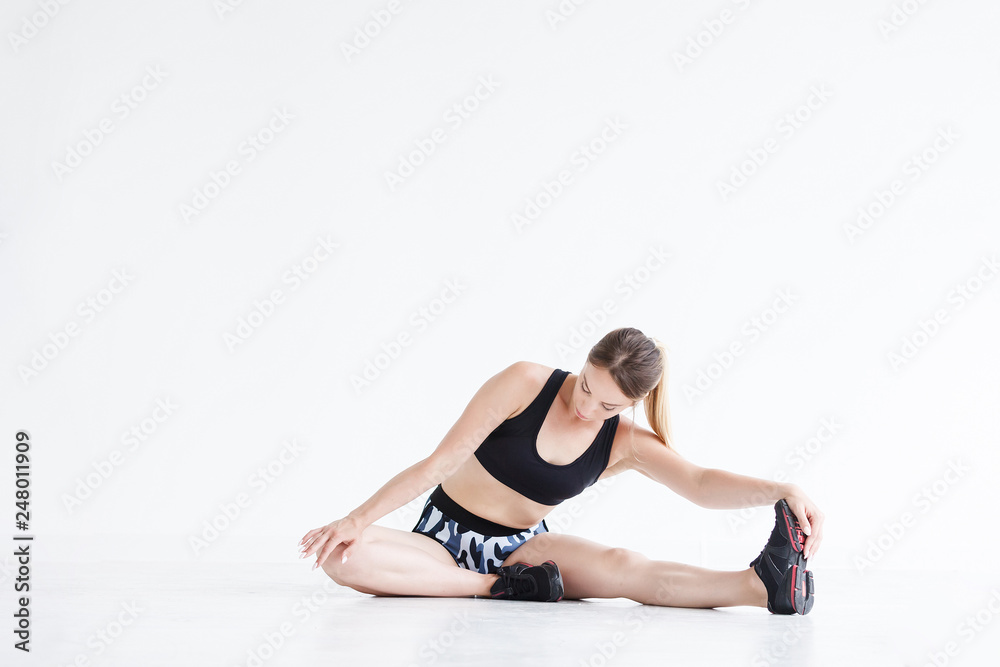 Beautiful young athletic girl doing exercises for stretching the ligaments and muscles of the legs before training sitting on the floor in the gym