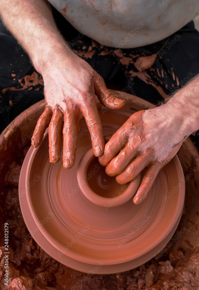 hands of potter creating a jar on circle