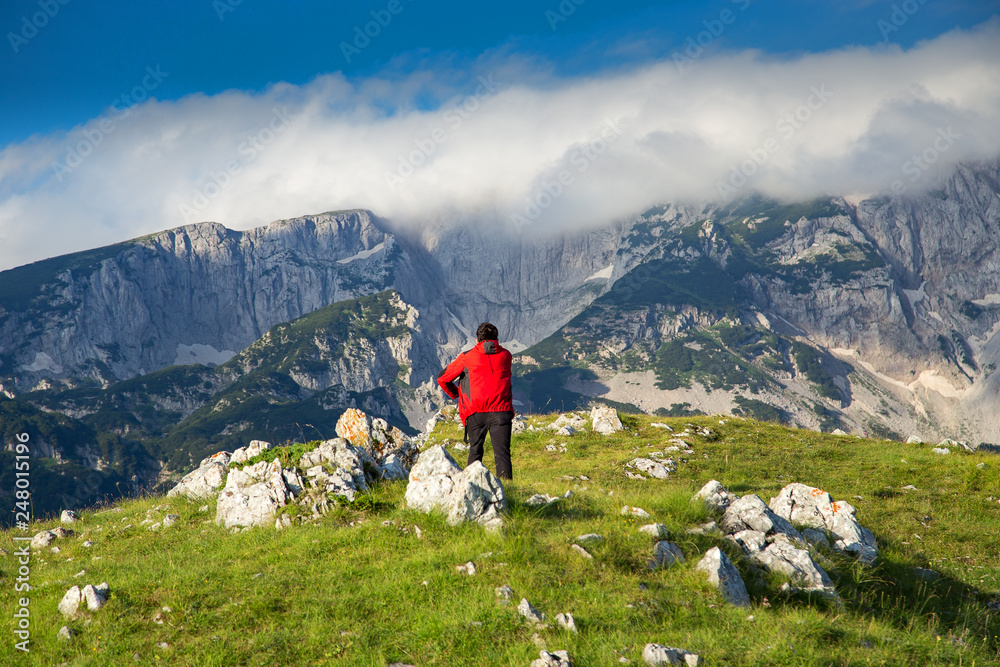 Hiker in red jacket enjoying at breathtaking view in mountain