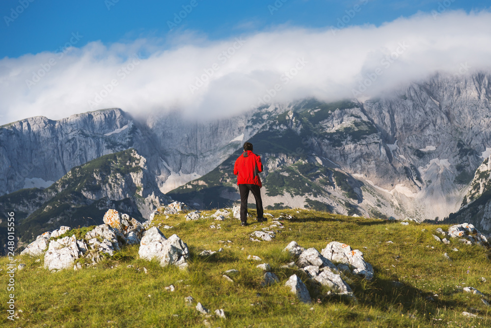 Hiker in red jacket enjoying at breathtaking view in mountain