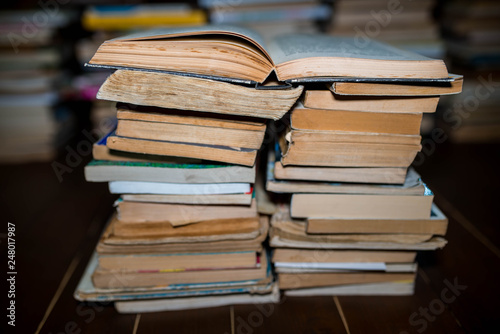 Opened book on columns of books, shallow depth of field, cracked wood floor.