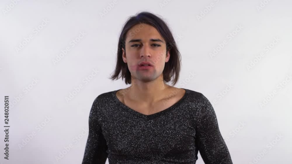 Portrait of handsome man smears lipstick on face in the studio. Transgender man in shiny dress removing makeup on white background. Drag queen isolated on a white background in the studio. Portrait of handsome man smears lipstick on face in the studio. Transgender man in shiny dress removing makeup on white background. Drag queen isolated on a white background in the studio.