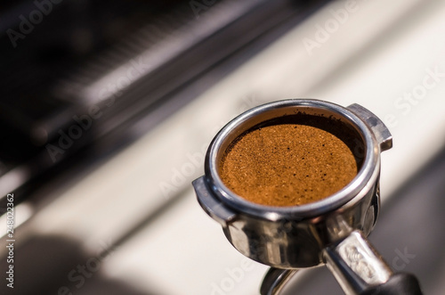 Fresh grinded roasted espresso coffee pressed in metal portafilter closeup.