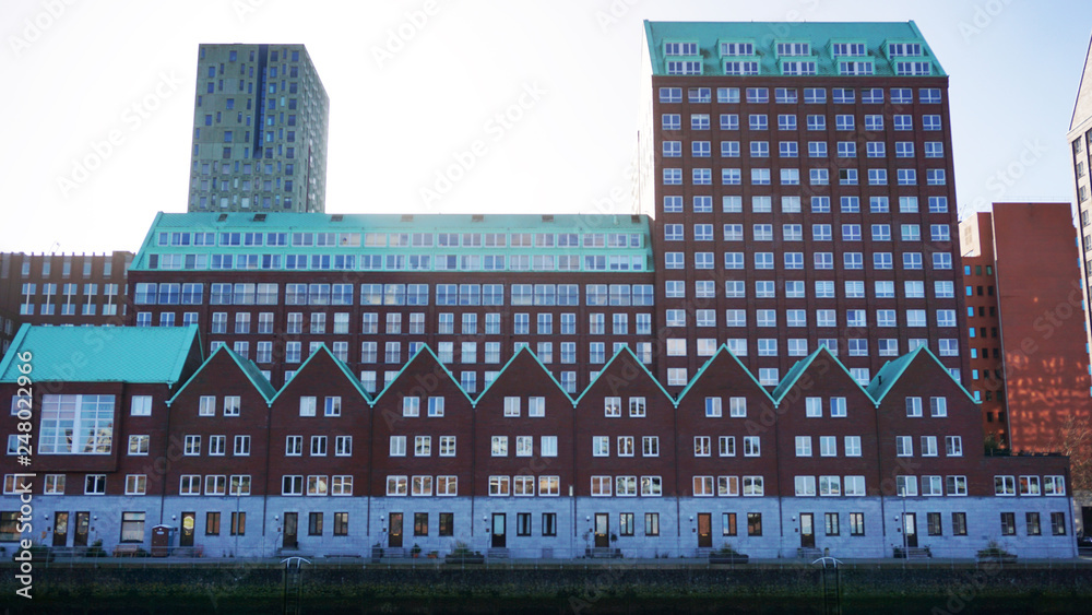 Modern brick red houses with triangular green roofs in the Kop van Zuid area of Rotterdam, the Netherlands. Cityscape, living area, many buildings and windows  together