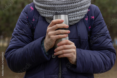 woman hands holding thermo cup of hot coffee on the forest background