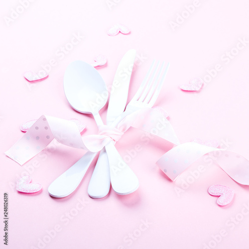 Festive table setting for Valentines Day with fork, knife and hearts on pink pastel background.Romantic dinner. Space for text.