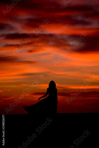 Silhouette of young woman with long dress at sunrise on the beach 