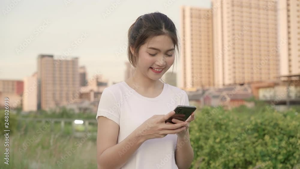 Cheerful Asian tourist blogger woman using touchscreen technology at smartphone while walking on the street at downtown city in the evening. Lifestyle backpack tourist travel holiday concept. Cheerful Asian tourist blogger woman using touchscreen technology at smartphone while walking on the street at downtown city in the evening. Lifestyle backpack tourist travel holiday concept.