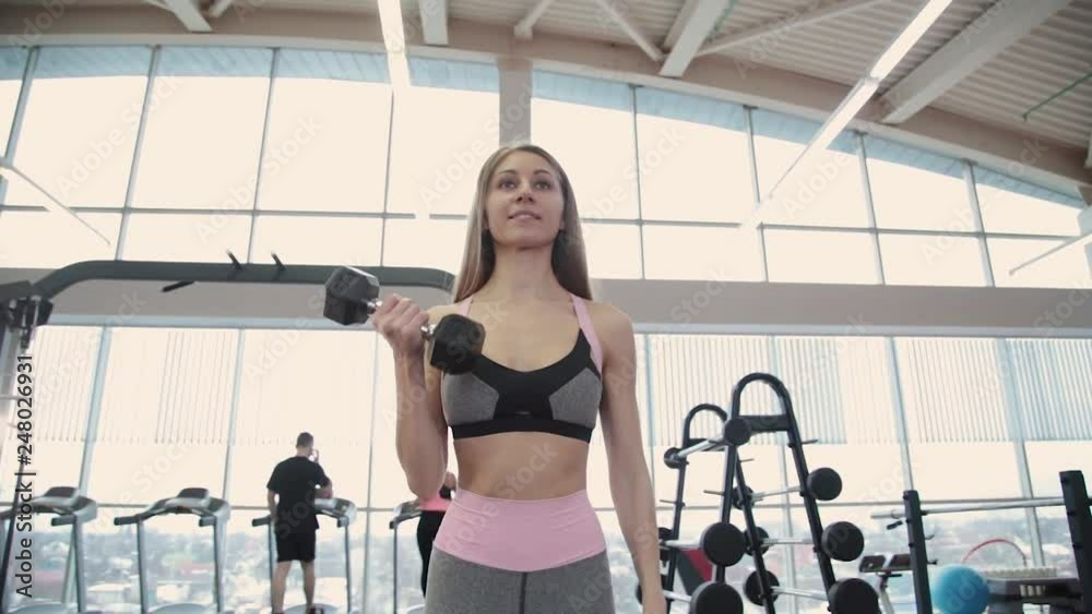 Beautiful athletic young girl trains dumbbells biceps in the gym. Beautiful athletic young girl trains dumbbells biceps in the gym.
