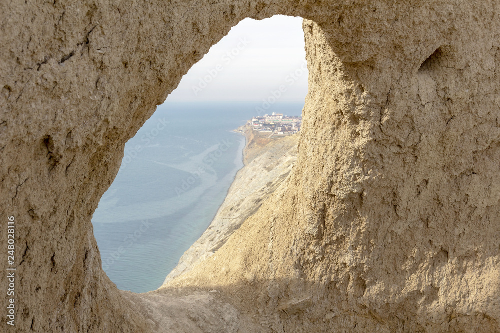 view through a round hole in the mountain to the sea and the city