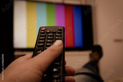 Remote control in hand before TV. Couch potato. Point of view shot. Woman holding remote control in hand.