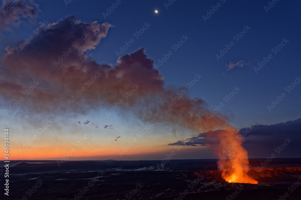 A view of an active volcano at dawn, with orange glow from the lava and the early morning sky in the background. It is the Kilauea volcano on Hawaii’s Big Island, before the 2018 eruption.