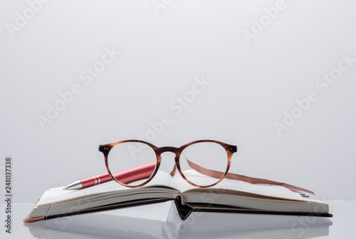 Diary planner opened book, reading glasses and pen with toned background