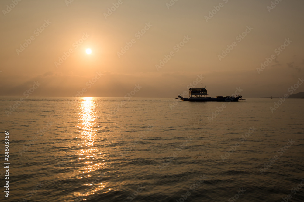 Ferry boat on the  Ocean  silhouetted against a setting sun and orange sky. Silhouette of the Ferry ship over the sunset Ferry float in the sea in the evening. International transportation, shipping, 