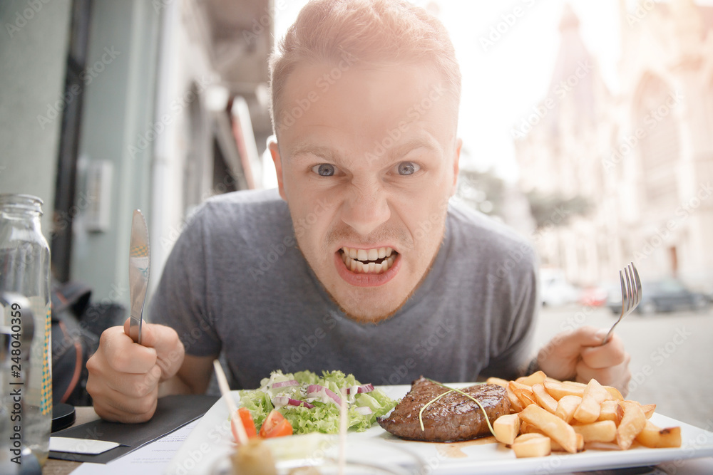 Very hungry man prepares to eat juicy steak and French fries, holds knife and fork