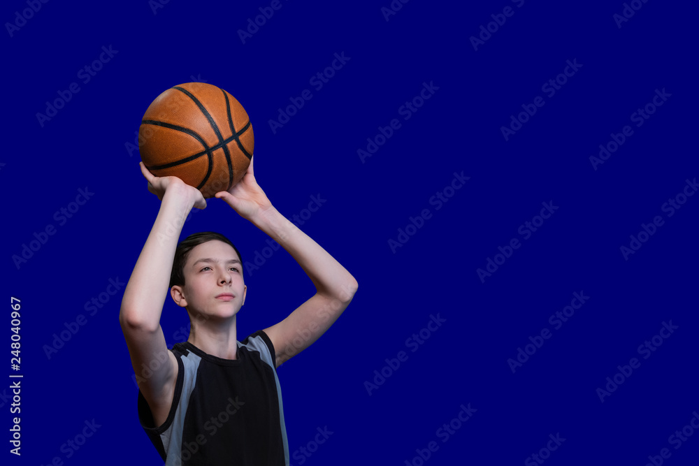 Teen in a black T-shirt is preparing to throw a basketball. Isolated on blue background. Copy space. Blank for sports poster.