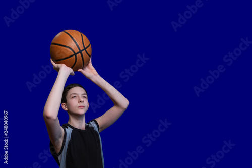 Teen in a black T-shirt is preparing to throw a basketball. Isolated on blue background. Copy space. Blank for sports poster.