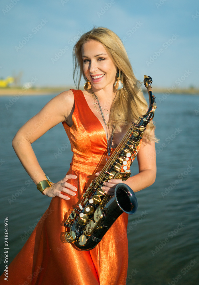 Girl with sax smiles, flirts. Happy blonde woman with big bust plays,  performs on goldy saxophone in beautiful dress Stock Photo | Adobe Stock