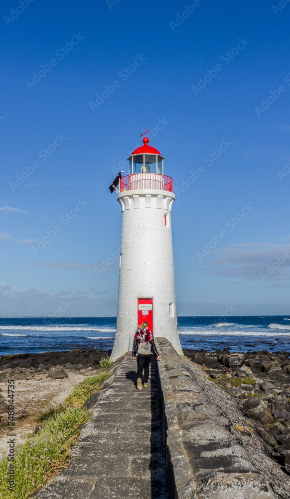 young woman dressed in black is walking towards a white lighthouse , Great Ocean Road