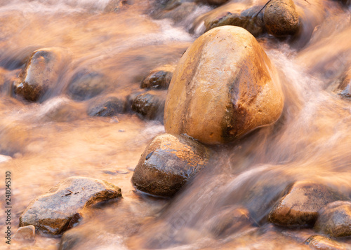 Water rushes around worn smooth rocks and over the sandy yellow bed of the river.