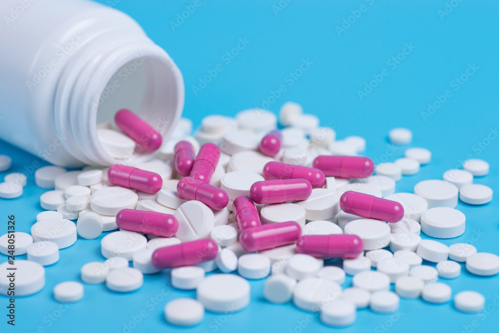 White and pink pills, tablets and white bottle on blue background.