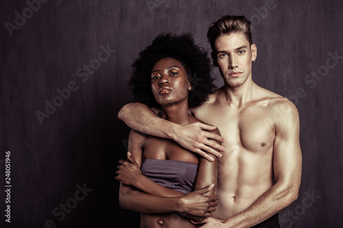 Beautiful multicultural couple standing together against grey background