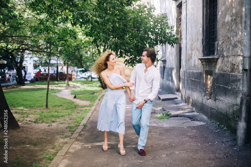 beautiful happy couple in love walking and gently hugging in sunny green street. stylish hipster groom and blonde bride embracing. romantic moments in summer city street on vacation