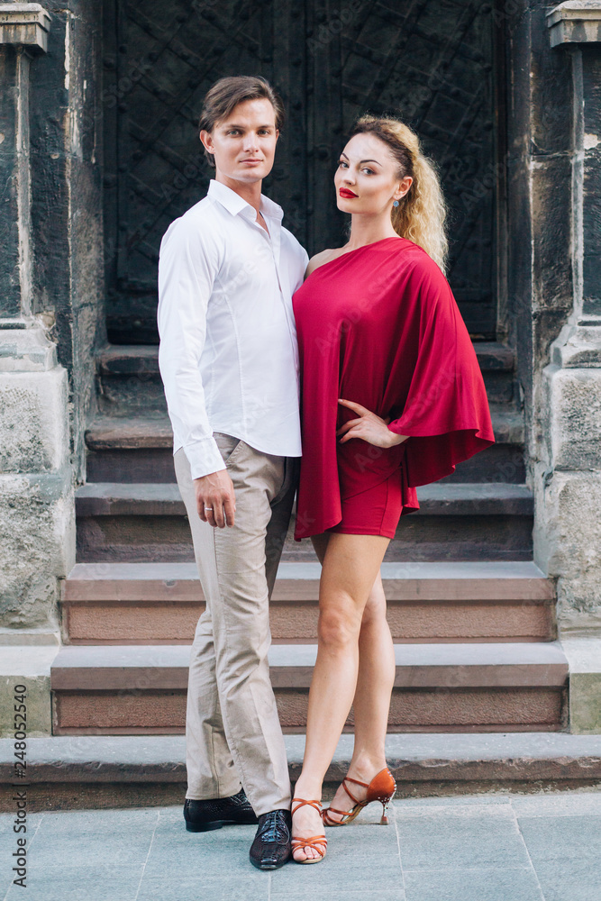 beautiful happy couple in love posing at old building in sunny street. stylish hipster groom and blonde bride in red dress gently hugging, professional dancers. romantic moments in summer beautiful happy couple in love posing at old building in sunny street. stylish hipster groom and blonde bride in red dress gently hugging, professional dancers. romantic moments in summer