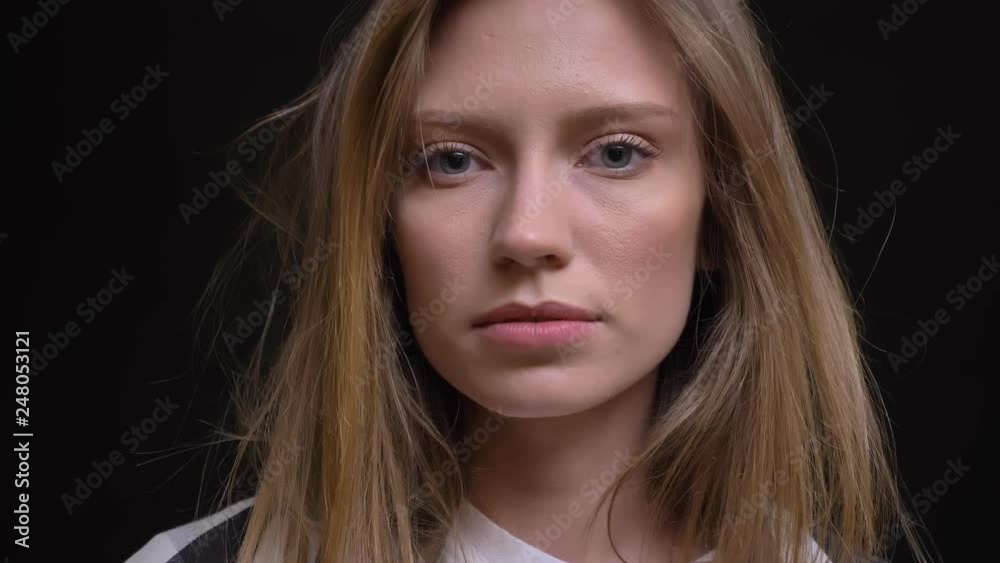Close-up portrait of young concentrated caucasian long-haired girl in shirt watching seriously into camera on black background. Close-up portrait of young concentrated caucasian long-haired girl in shirt watching seriously into camera on black background.