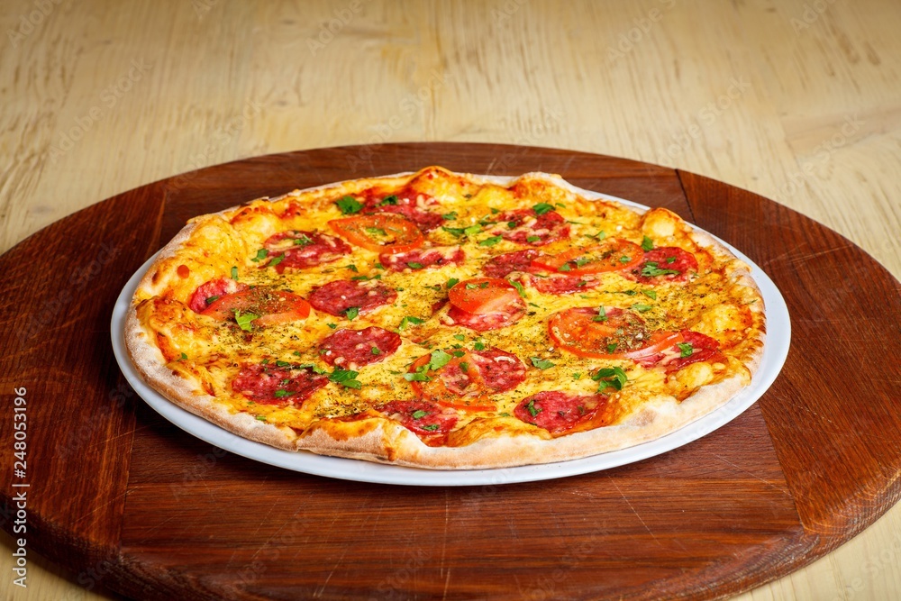 Pizza Italian pepperoni with melted cheese, salami, tomatoes and species on a white plate on a thick brown table
