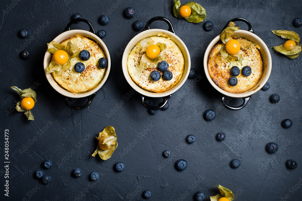 Three portions of classic English rice pudding. Blueberries and physalis. Dark background, top view, space for text
