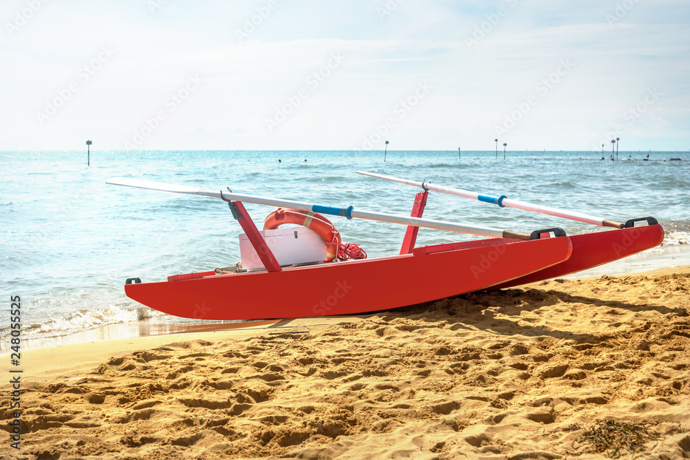 red wooden rescue boat with oars and a lifeline on the seafront on a sandy beach red wooden rescue boat with oars and a lifeline on the seafront on a sandy beach