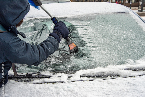 Man cleaning car windshield from ice with scraper tool.