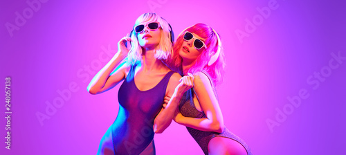 Fashion. Two DJ girl with Dyed Hair, party makeup in Colorful neon light enjoy music, friends. Disco 80s 90s vibes. Model woman in fashionable bodysuit, make up dancing. Art uv neon banner