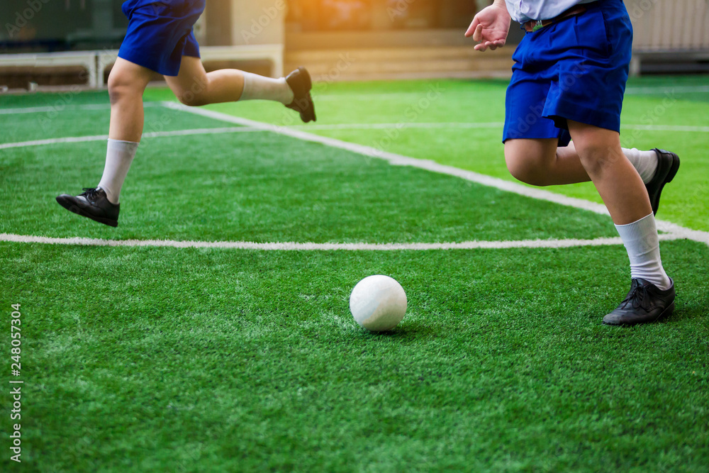 Asian student play plastic soccer ball on green artificial turf