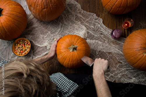 Man carving Halloween jack-o-lantern with a knife surrounded by pumpkins. 